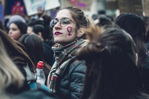 A woman marching at a protest with her face painted with the symbol for women