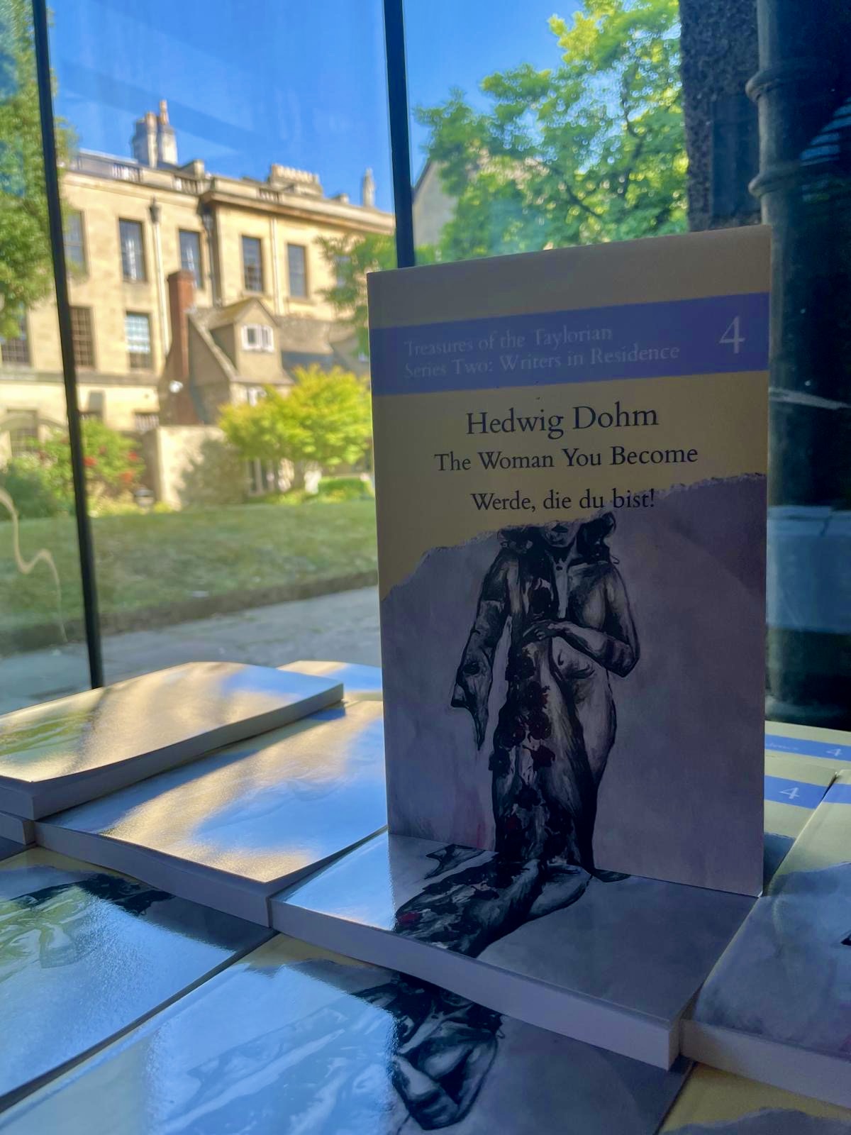 Copy of "The Woman You Become" standing upright to show the cover, with a beautiful building in the background through a window